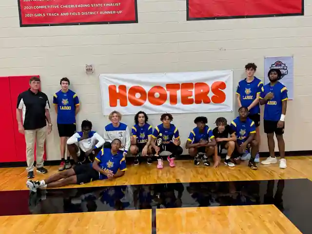 Largo basketball team with their trophy in front of the Hooters banner at the 2023 Tampa Bay Sportsmanship Classic